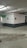 A concrete parking garage corner with visible structural elements, featuring directional exit signs on the walls. The environment appears slightly worn with visible moisture on the ground and overhead lighting. Pipes and conduits are attached to the ceiling.