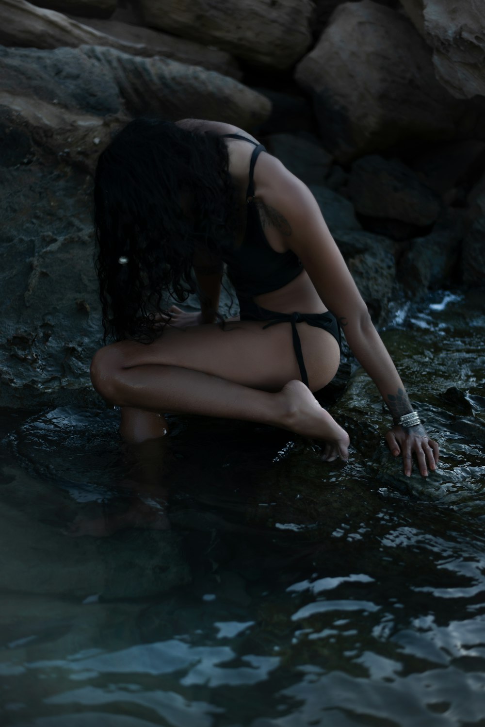 a woman in a black bikini sitting in a body of water