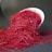 Bright red saffron threads are spilling out of a tilted white bowl onto a dark surface. The fine, delicate threads create a vivid contrast against the dark background.