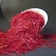Bright red saffron threads are spilling out of a tilted white bowl onto a dark surface. The fine, delicate threads create a vivid contrast against the dark background.