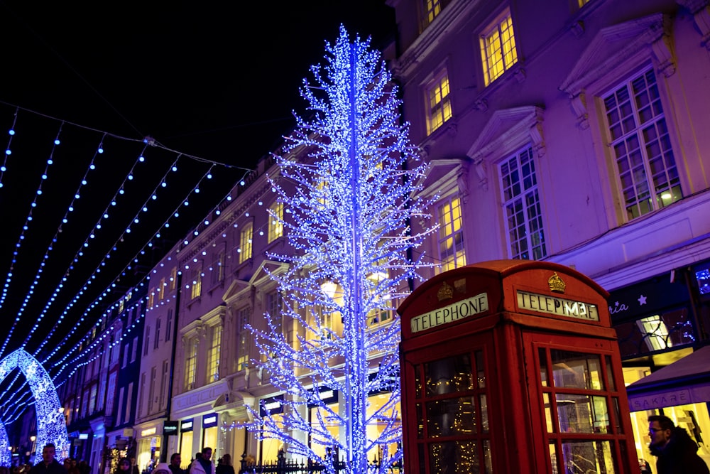 uma árvore de Natal azul e uma cabine telefônica vermelha