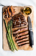 A beautifully grilled steak on a wooden cutting board with herbs and spices around it.