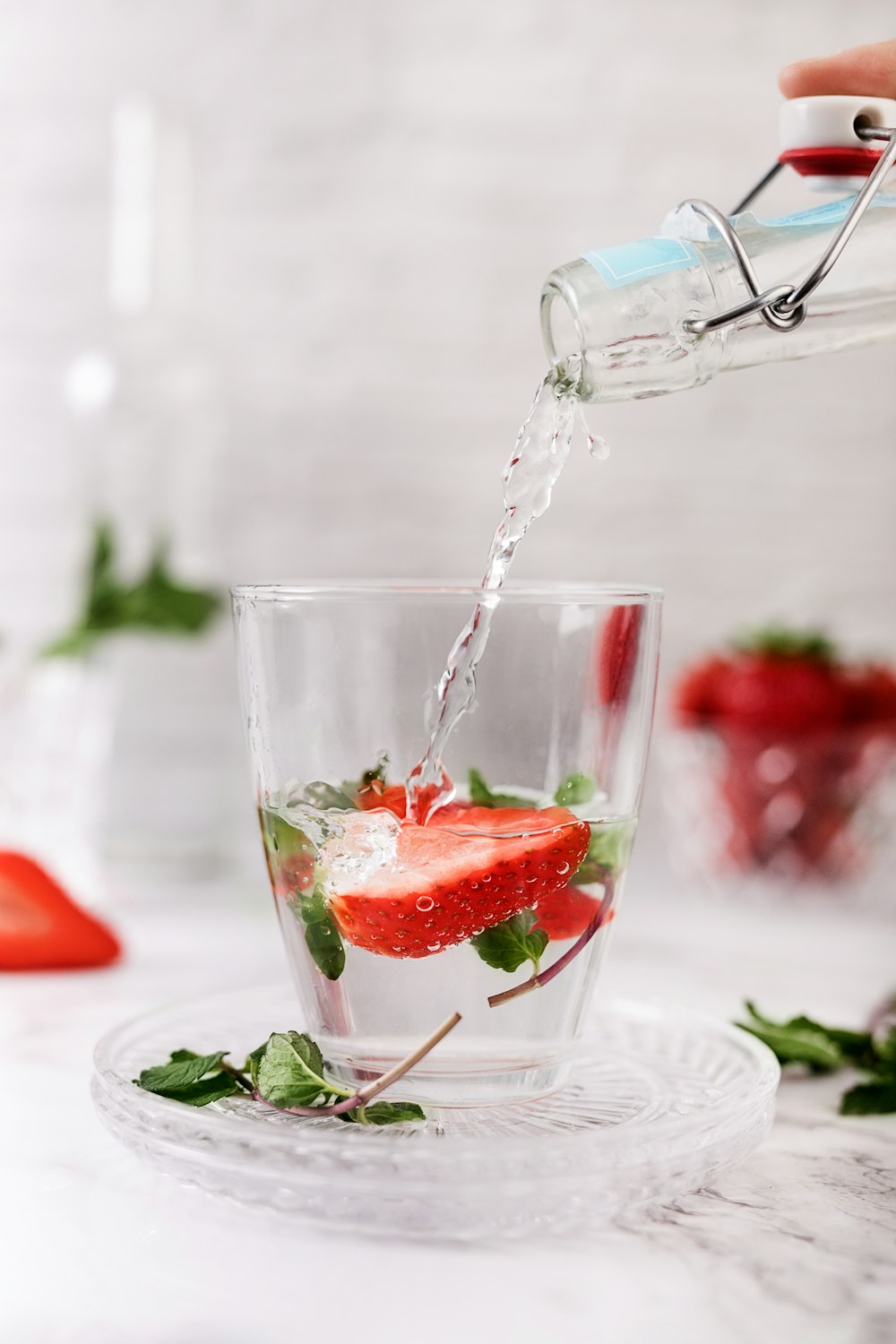 a person pouring water into a glass filled with strawberries