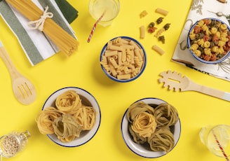 three bowls of pasta sit on a yellow surface