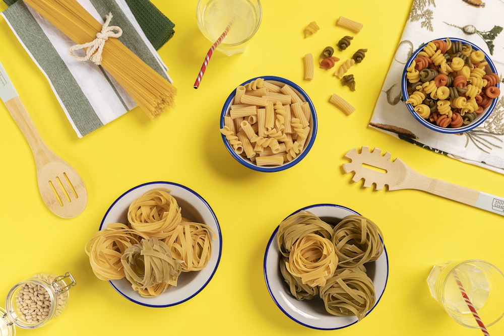 three bowls of pasta sit on a yellow surface