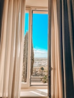 A serene window view framed by flowing curtains, overlooking a quiet garden.
