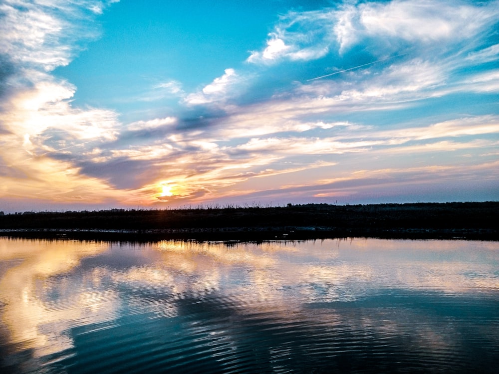 the sun is setting over a calm lake