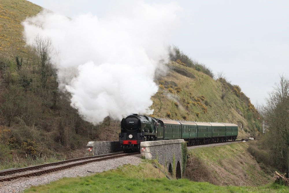 a train traveling down tracks next to a lush green hillside