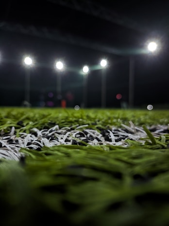 Close-up of a football ball spinning on the grass with stadium lights in the background.