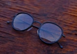 Close-up of sleek black-rimmed eyeglasses resting on a wooden table.