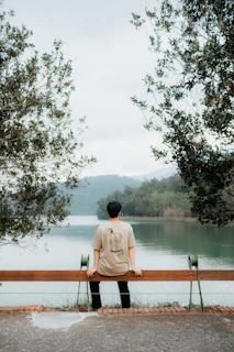 A serene outdoor shot of Kentenfromlucca sitting on a bench, composing music with a notebook.