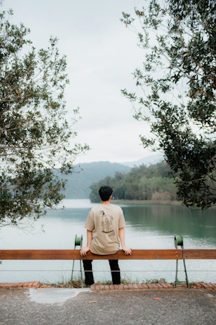 A serene outdoor shot of Kentenfromlucca sitting on a bench, composing music with a notebook.