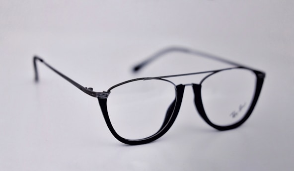 A pair of black-rimmed eyeglasses with a sleek and modern design. The glasses are placed on a plain light background, highlighting their stylish shape and glossy finish.