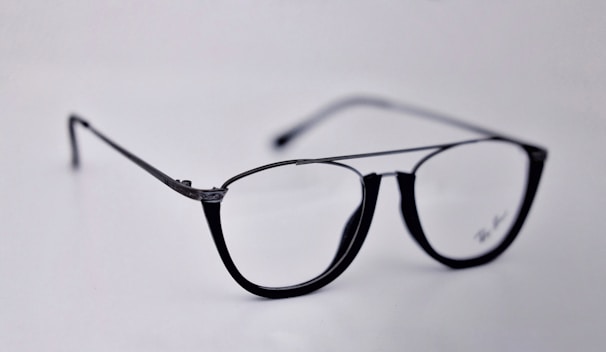 A pair of black-rimmed eyeglasses with a sleek and modern design. The glasses are placed on a plain light background, highlighting their stylish shape and glossy finish.