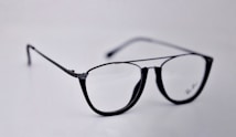 A pair of black-rimmed eyeglasses with a sleek and modern design. The glasses are placed on a plain light background, highlighting their stylish shape and glossy finish.