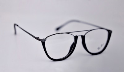 A pair of black-rimmed eyeglasses with a sleek and modern design. The glasses are placed on a plain light background, highlighting their stylish shape and glossy finish.