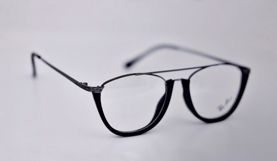 A pair of black-rimmed eyeglasses with a sleek and modern design. The glasses are placed on a plain light background, highlighting their stylish shape and glossy finish.
