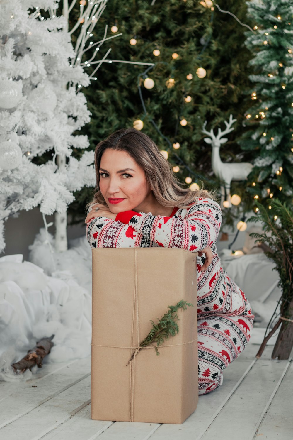 a woman sitting on the floor with a christmas present in front of a christmas tree