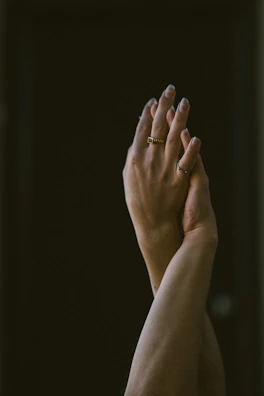 A hand wearing a minimalist silver ring, fingers softly curled against a blurred neutral background.