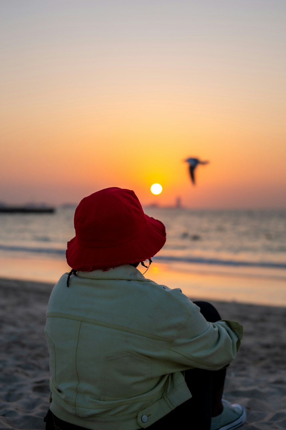 Una persona sentada en una playa mirando la puesta de sol