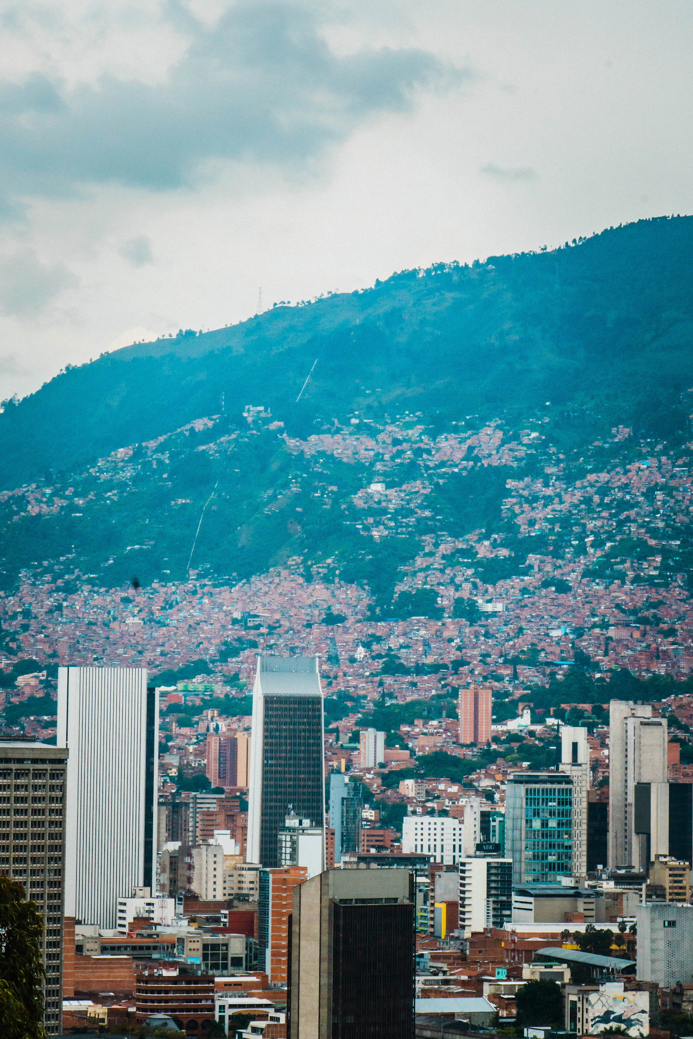 Medell&iacute;n Colombia city downtown with tall buildings in the valley and the massive green Andes mountains rising steeply behind the urban skyline