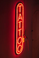 Bright neon flex logo sign for a tattoo studio, mounted on a dark textured wall.
