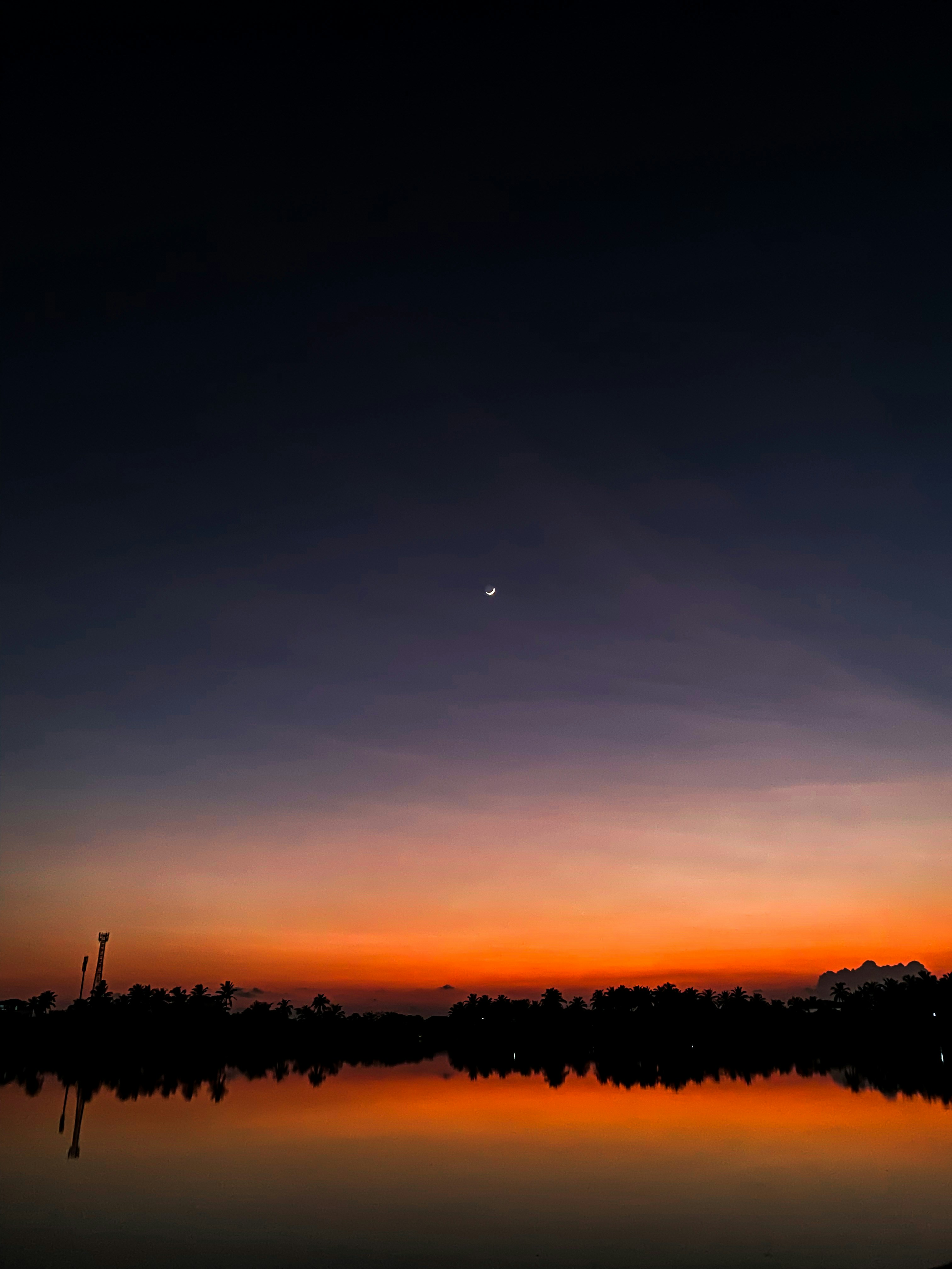 Dark moody night sky with crescent moon over still water, deep indigo atmosphere, dim starlight, atmospheric shadows