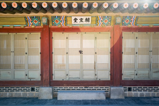 A traditional Korean building facade with intricately designed wooden doors and vibrant colorful patterns above, featuring traditional Korean roof tiles and decorative floral motifs.