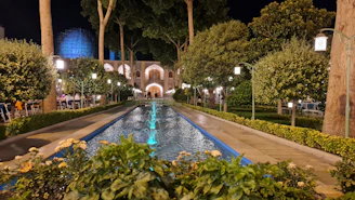 A beautifully landscaped garden featuring a stone fountain and illuminated pillars at dusk.
