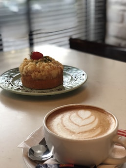 A cup of coffee with latte art sits on a table next to a dessert decorated with a strawberry, creating an inviting and cozy atmosphere in a cafe setting.