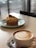 A cup of coffee with latte art sits on a table next to a dessert decorated with a strawberry, creating an inviting and cozy atmosphere in a cafe setting.