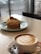 A cup of coffee with latte art sits on a table next to a dessert decorated with a strawberry, creating an inviting and cozy atmosphere in a cafe setting.