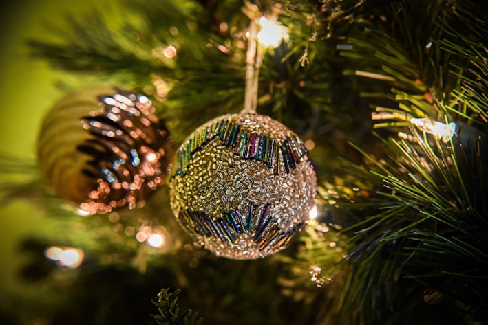 A close-up of a beautifully detailed handmade Christmas ornament hanging on a pine tree.