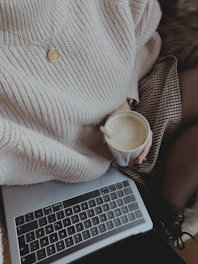 a woman is holding a cup of coffee while using a laptop