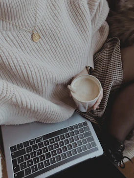 a woman is holding a cup of coffee while using a laptop