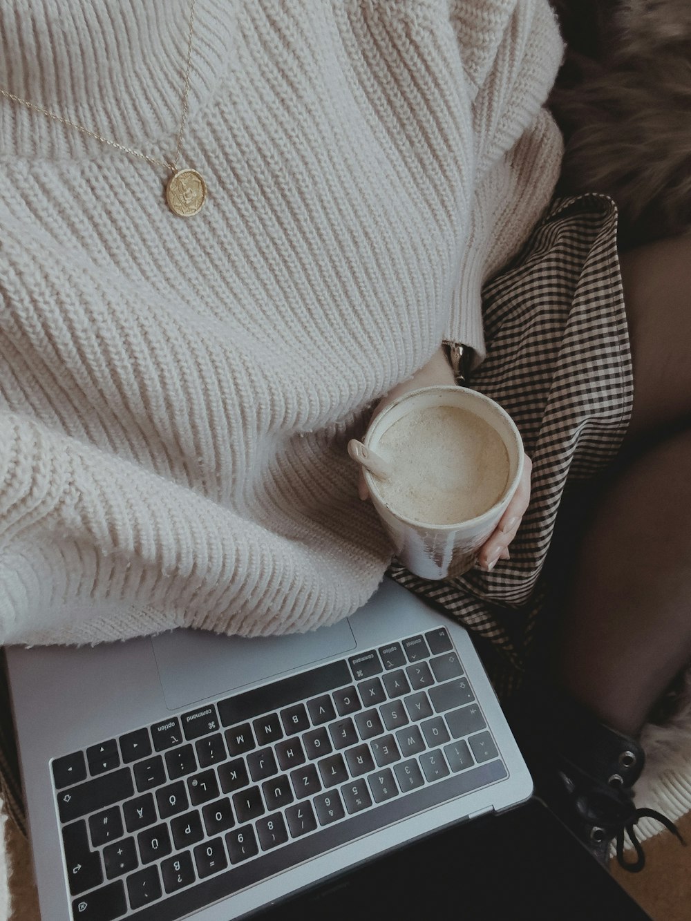 a woman is holding a cup of coffee while using a laptop