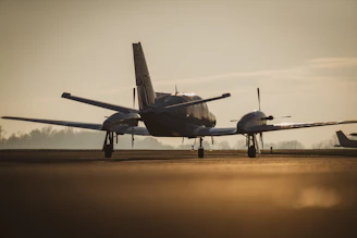 A small aircraft lifting off a runway bathed in the soft golden light of sunrise, with a pilot visible through the cockpit window.
