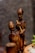 Wooden sculptures depict two figures with elongated features and a polished dark surface. One figure is seated, holding a stick, while the other stands nearby. They appear to be carved from a single piece of wood.