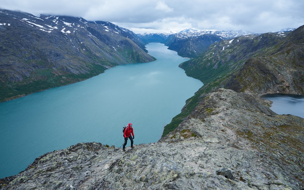 a man standing on top of a mountain next to a lake