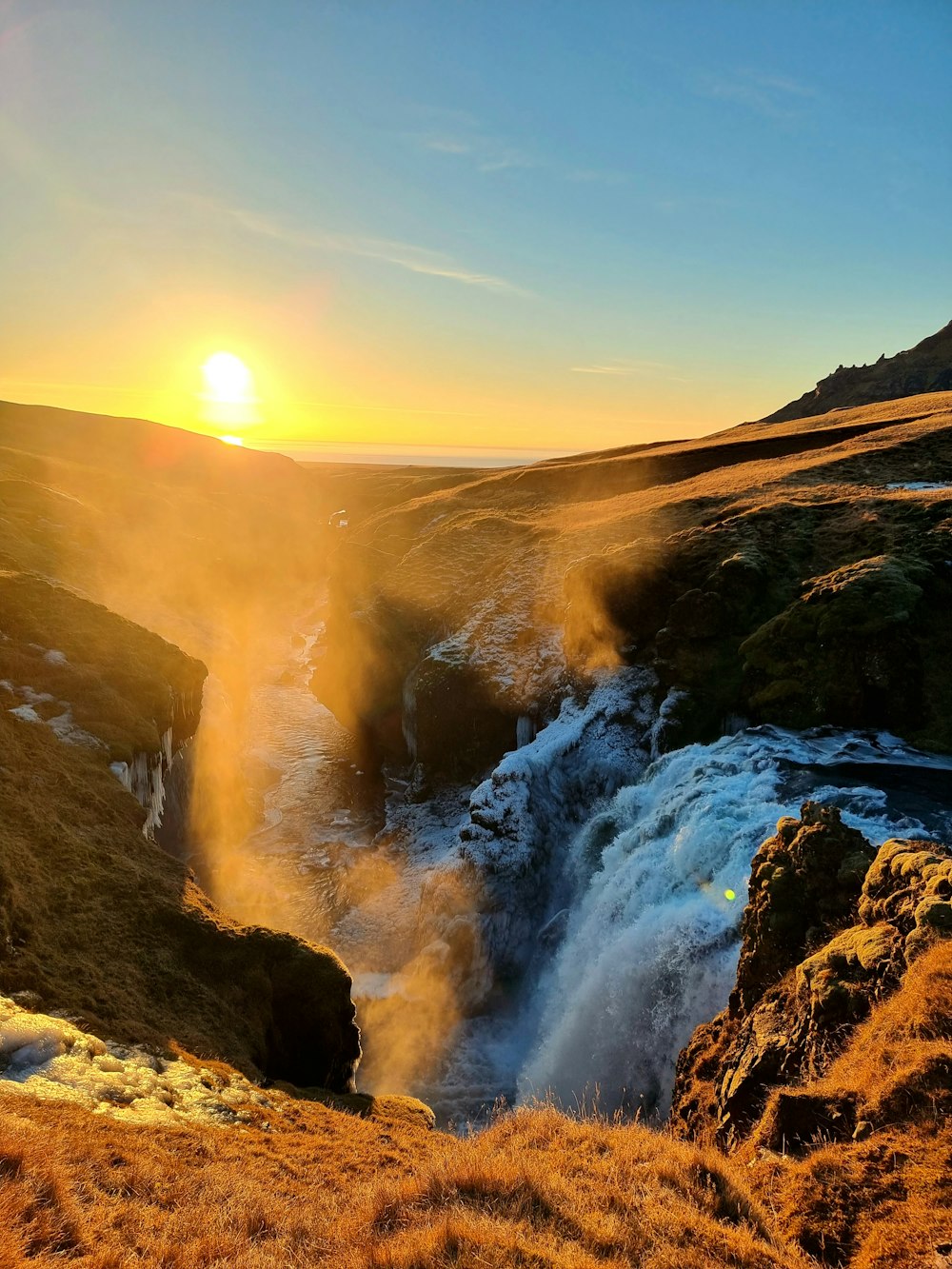 the sun is setting over a waterfall in the mountains