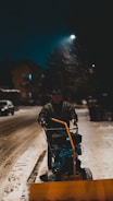 A snow removal worker using a snow blower on a residential driveway early in the morning.