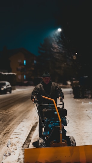 A snow removal professional using a snow blower on a residential driveway early in the morning.