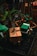 A festive arrangement of wrapped gift boxes with colorful ribbons is placed on a wooden platform. The scene is adorned with a small palm plant and set against a dark background, enhancing the vibrant colors of the gifts.
