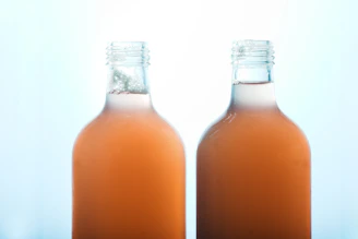 A clear bottle of mouthwash with bubbles inside, placed next to a glass on a green and white background.