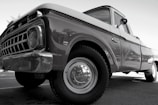 A classic vintage truck with a shiny surface and detailed front grille, viewed from a low angle emphasizing its robust build. The truck appears well-maintained with visible reflections on its body, highlighting the contours and craftsmanship of its era.