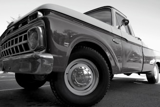 A classic vintage truck with a shiny surface and detailed front grille, viewed from a low angle emphasizing its robust build. The truck appears well-maintained with visible reflections on its body, highlighting the contours and craftsmanship of its era.