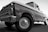 A classic vintage truck with a shiny surface and detailed front grille, viewed from a low angle emphasizing its robust build. The truck appears well-maintained with visible reflections on its body, highlighting the contours and craftsmanship of its era.