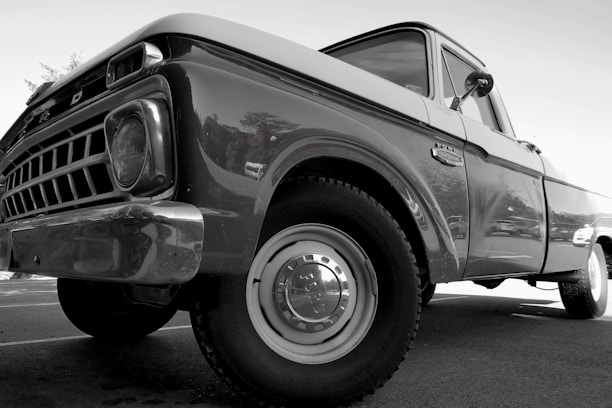 A classic vintage truck with a shiny surface and detailed front grille, viewed from a low angle emphasizing its robust build. The truck appears well-maintained with visible reflections on its body, highlighting the contours and craftsmanship of its era.