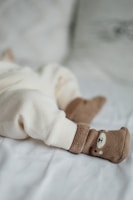 A cozy scene with a baby's legs dressed in soft cream-colored, textured pants lying on a light blanket. The feet are adorned with adorable brown socks featuring a cute bear face design.