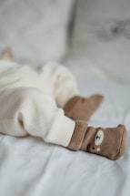 A cozy scene with a baby's legs dressed in soft cream-colored, textured pants lying on a light blanket. The feet are adorned with adorable brown socks featuring a cute bear face design.